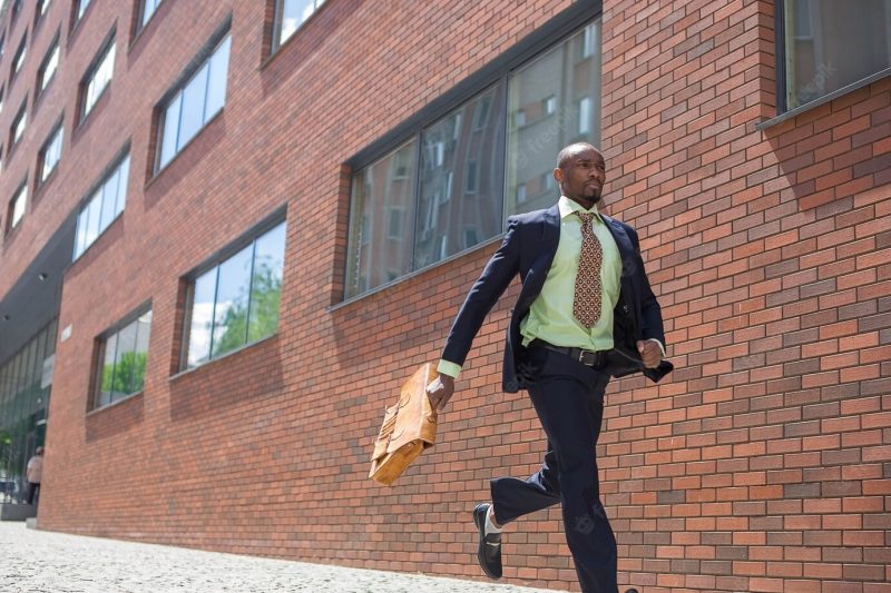 The African man as black businessman with a briefcase running in a city street on a background of red brick wall Free Photo