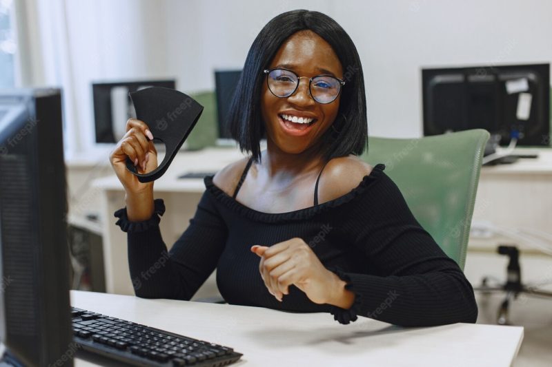 African woman sitting in computer science class. lady in glasses smiles at the camera. female student sitting at the computer. Free Photo