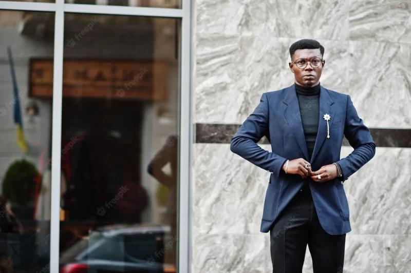 Amazingly looking african american man wear at blue blazer with brooch black turtleneck and glasses posed at street fashionable black guy Free Photo