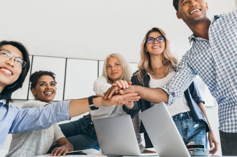 Asian businessman in leather wristwatch holding hands with partners and smiling. indoor portrait of team of office workers having fun before big project. Free Photo