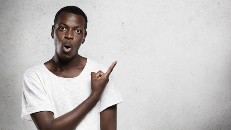 Astonished dark-skinned customer or employee pointing his finger at blank wall Free Photo