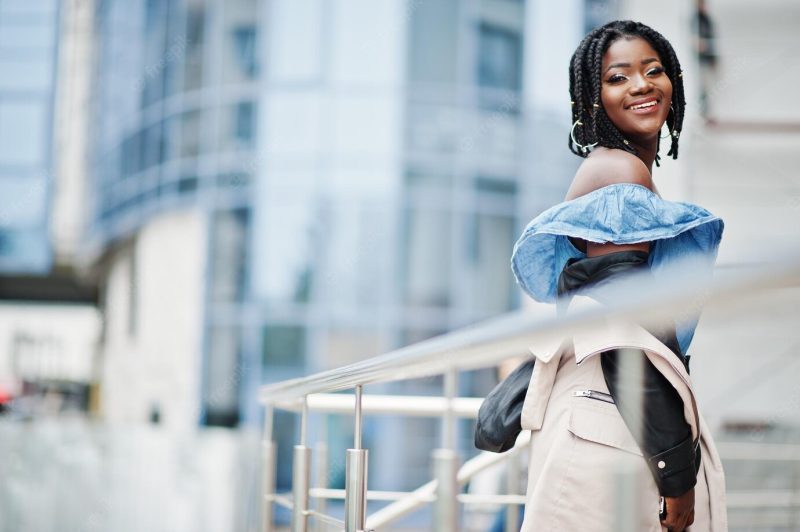 Attractive african american woman with dreads in jacket posed near railings against modern multistory building Free Photo