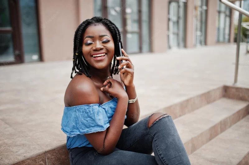 Attractive african american woman with dreads in jeans wear sitting on stairs with mobile phone Free Photo