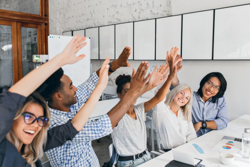 Attractive european woman waving hands with friends, happy for successful meeting. african and asian office workers having fun during conference and laughing. Free Photo