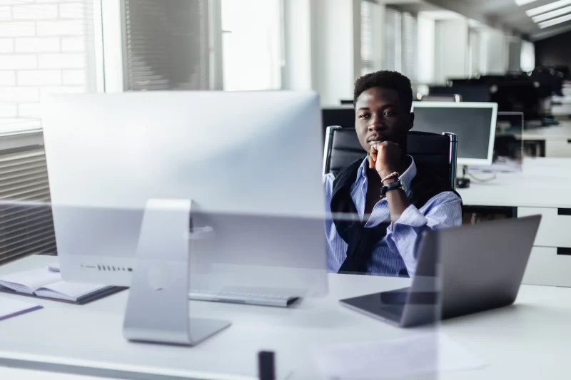 Attractive hardworking young afro-american office worker sitting at desk in front of open laptop pc and making notes. Free Photo