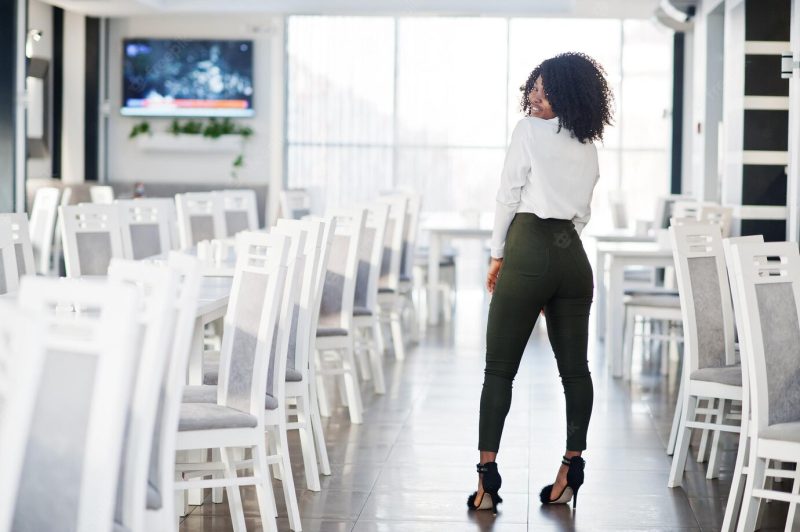 Back of cheerful sexy business African American lady with afro hair wear white blouse and green pants posed in cafe Free Photo