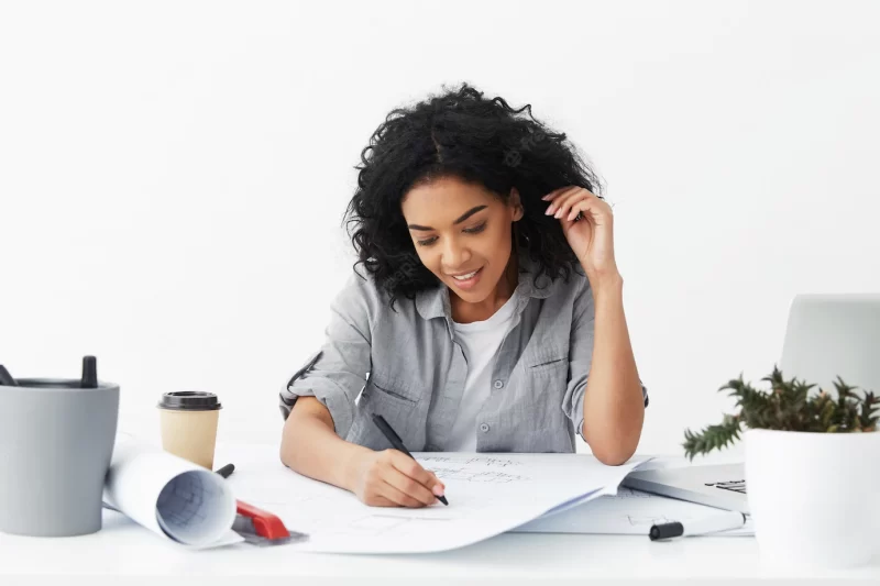 Beautiful young African American woman architect with black curly hair drawing sketch using pen Free Photo