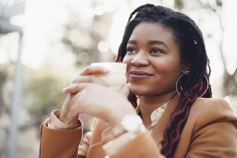 Beautiful young african american woman sitting in outdoor cafe and drinking coffee Free Photo