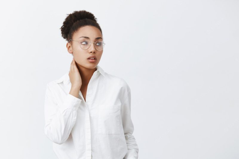 Being great boss tiresome. stylish and tender African-American female office worker in glasses and white shirt, touching neck and gazing with dreamy tired expression right, feeling pain in neck Free Photo