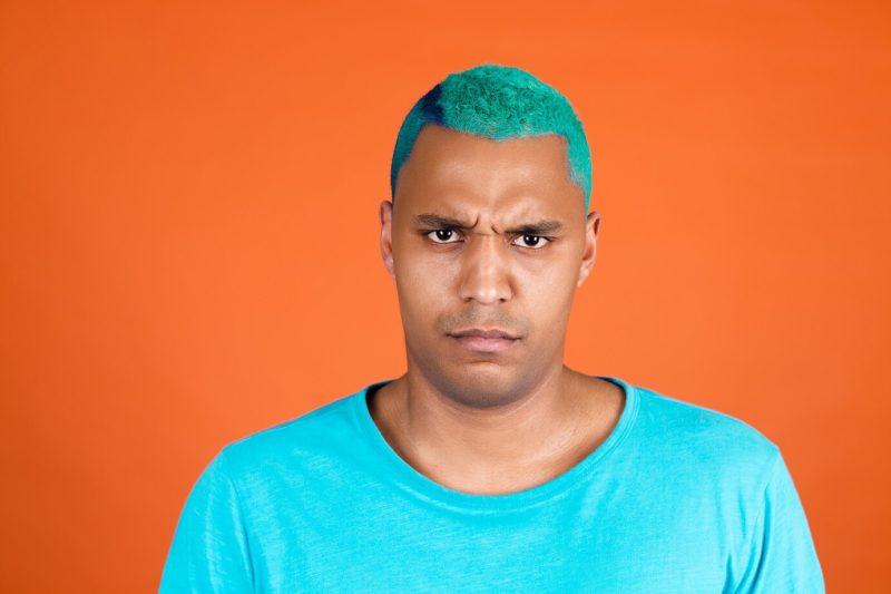 Black african man in casual on orange wall blue hair frowns disagree disappointed serious Free Photo