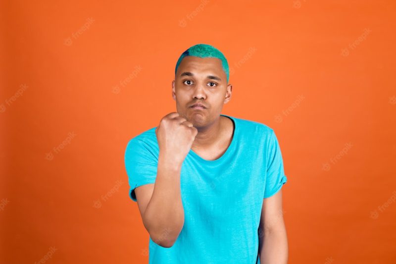 Black african man in casual on orange wall blue hair shouting angry raising fist unhappy and aggressive Free Photo