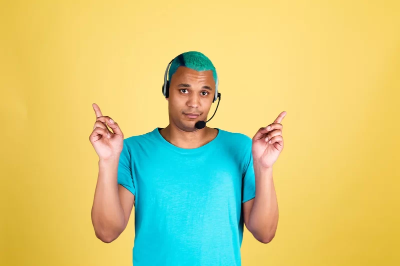 Black african man in casual on yellow wall blue hair call centre worker happy customer support operator with headphones point fingers up Free Photo