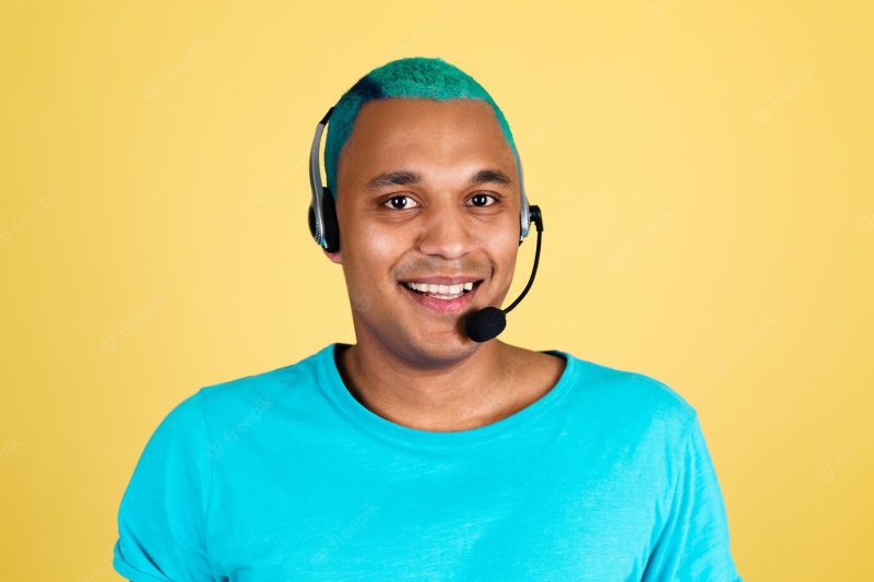 Black african man in casual on yellow wall blue hair call centre worker happy customer support operator with headphones Free Photo