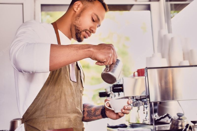 Black bearded coffee seller pouring coffee in a shop. Free Photo