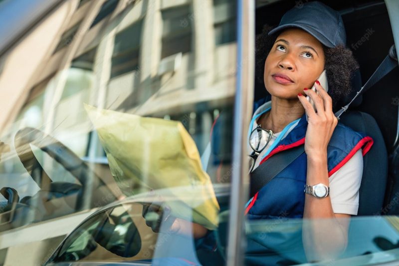 Black female courier communicating on mobile phone while delivering packages with a van Free Photo