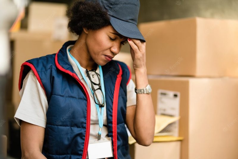 Black female courier holding her head in pain while delivering packages Free Photo