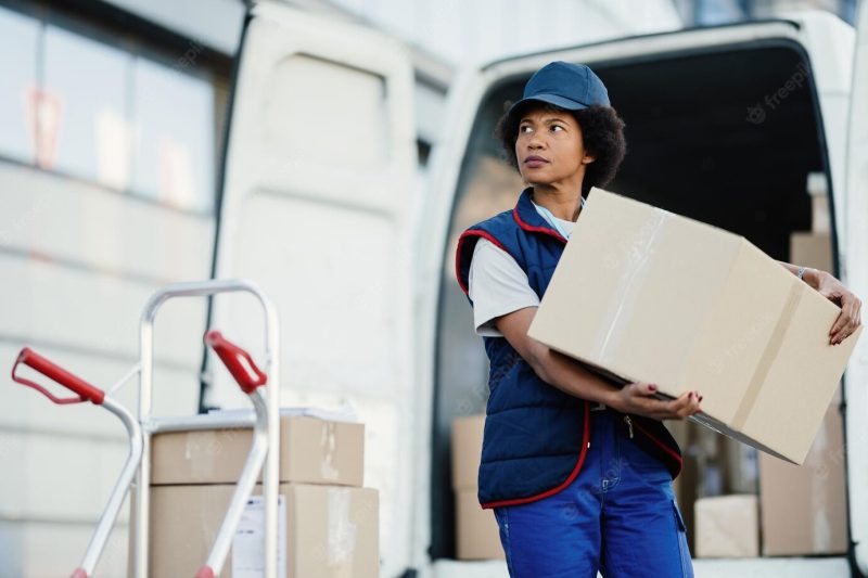 Black female courier unloading cardboard boxes from a van while making a delivery in the city Free Photo