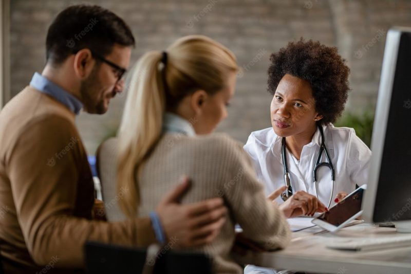 Black female doctor showing to a couple their electronic medical record on touchpad while communicating with them at clinic Free Photo