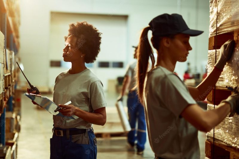 Black female inspector with walkietalkie checking stock of products while working in a warehouse Free Photo