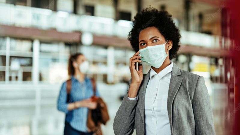 Black female passenger talking on smart phone while wearing face mask at the airport during virus epidemic Free Photo