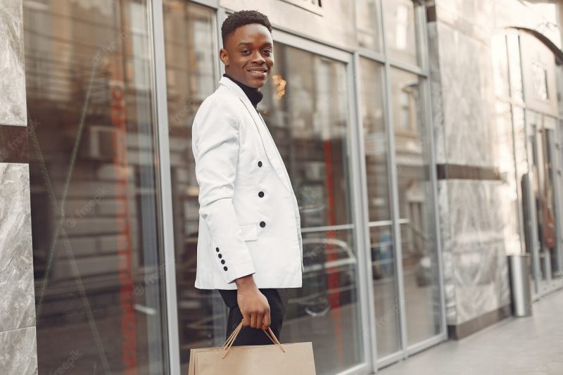 Black man in a white jacket with shopping bags Free Photo