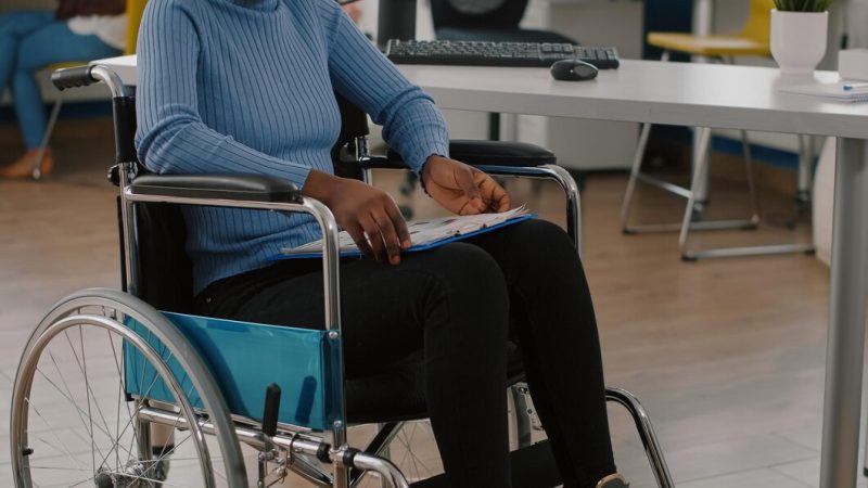 Black woman with disabilities, invalid, disabled paralized handicapped sitting immobilized in wheelchair holding clipboard with financial documents. african manager working in business office room Free Photo