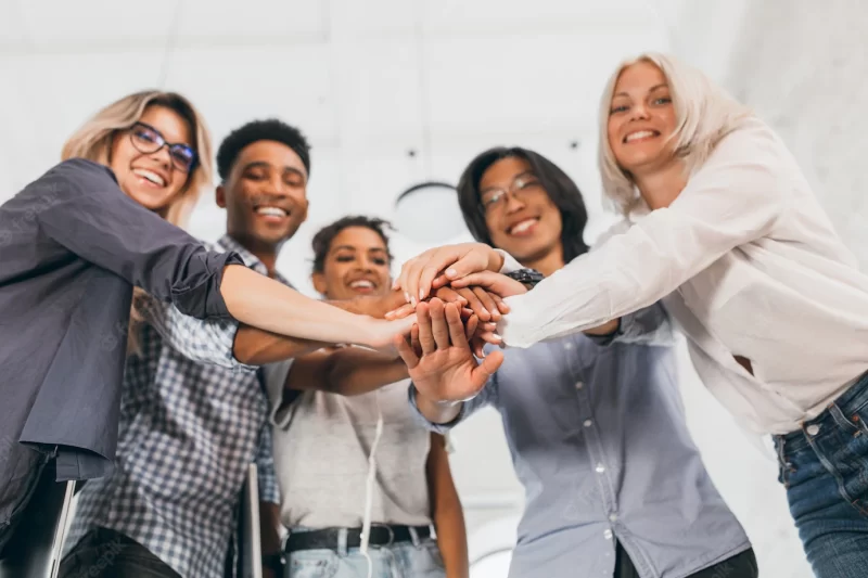 Blur portrait of team of young office workers with their hands in focus. indoor photo of laughing international students in stylish attires supporting each other before exams. Free Photo