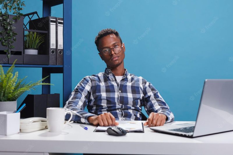 Bored and tired young adult business person sitting at office desk while looking at camera. exhausted and fatigued agency employee with boredom face expression sitting in workspace interior. Free Photo