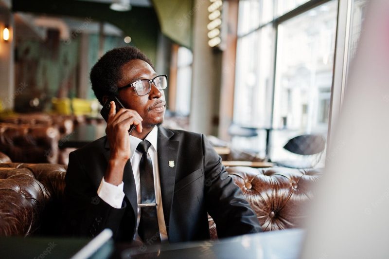 Business african american man wear on black suit and glasses sitting at office and speaking on phone behind laptop Free Photo