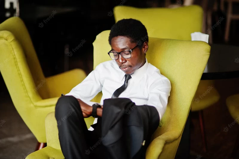 Business african american man wear on white shirt tie and glasses at office sitting on chair and looking at watches Free Photo