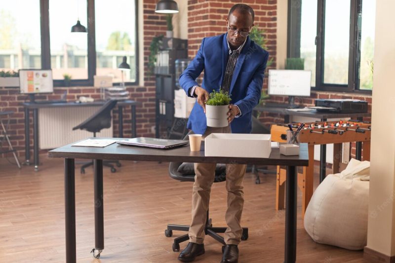 Business man packing up office things in box after getting fired from work. discharged person being dismissed from job and gathering belongings to leave startup company workplace. Free Photo