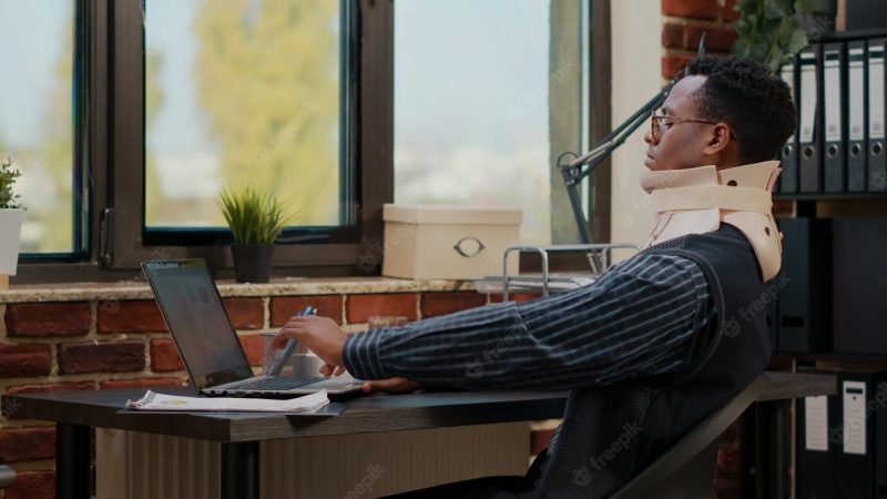 Business man wearing cervical neck collar at work after vertebrae injury in startup office. injured employee using medical foam while he works with laptop to plan commercial investment. Free Photo