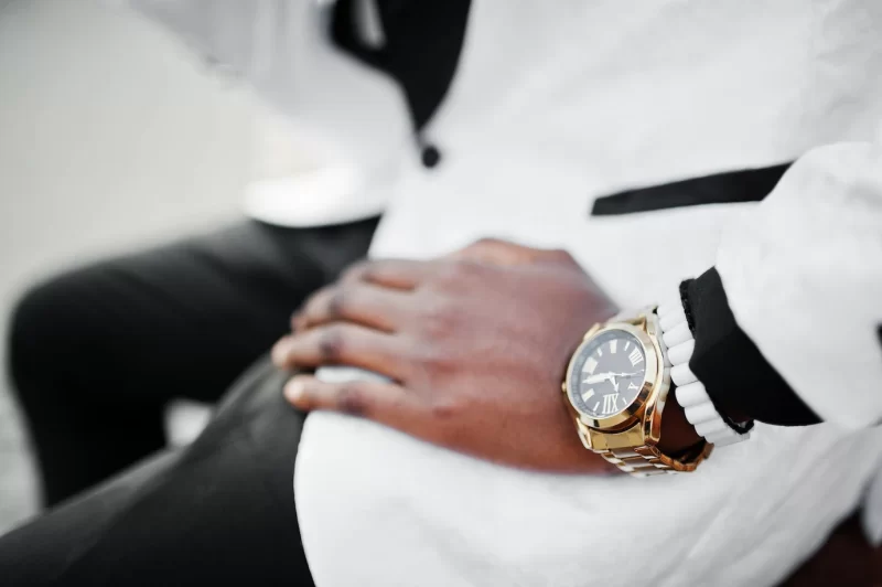 Chic handsome african american man in white suit sitting on bench close up photo of golden watches on hand Free Photo