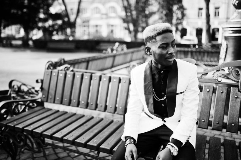 Chic handsome African American man in white suit sitting on bench Free Photo