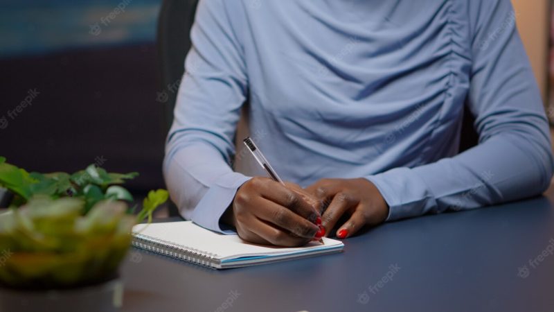 Close up of african businesswoman writing list of tasks for business project in notebook sitting at desk in living room working overtime. black freelancer respecting deadline studying late at night Free Photo