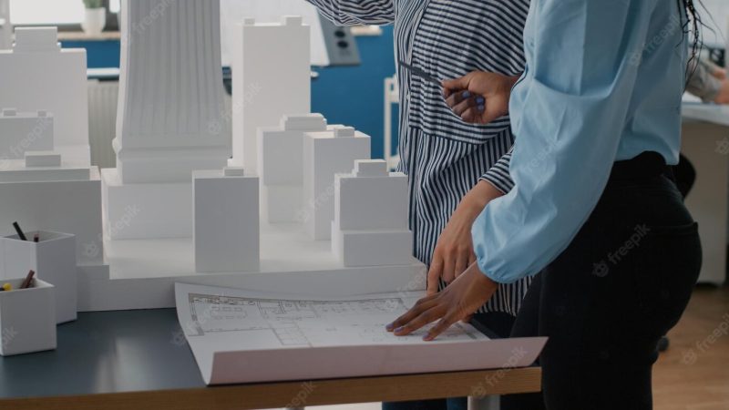 Close up of architects placing blueprints plan on table to work on urban project with building model. team of women using layout print to design construction structure and development. Free Photo