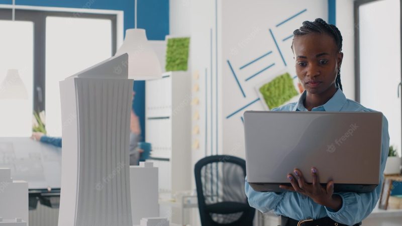 Close up of engineer looking at laptop to analyze building model in architectural office. woman builder using computer and maquette to design construction layout for development. Free Photo