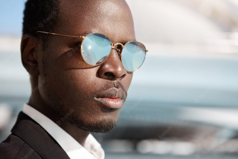 Close up highly-detailed shot of handsome serious Afro American office worker in formal wear and mirrored lens shades posing in urban surroundings, thinking about prospects and possibilities at work Free Photo