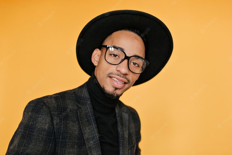 Close-up portrait of mulatto male model in black hat. indoor photo of cheerful young man with brown skin. Free Photo