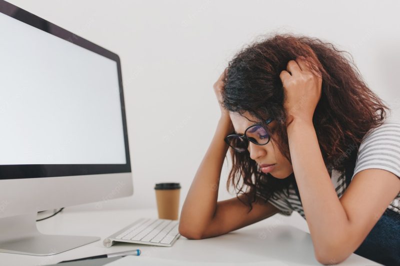 Close-up portrait of sad young woman lies near computer with white screen and cup of coffee Free Photo