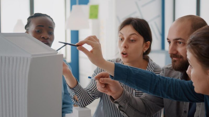 Close up of workmates analyzing building model and maquette on table to design construction. group of diverse colleagues working on architecture project for structure and development. Free Photo