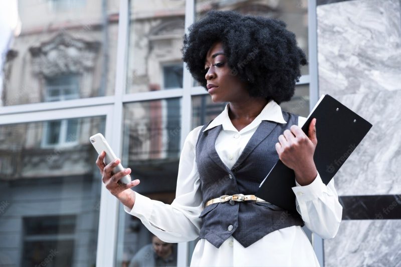 Close-up of a young african businesswoman holding clipboard using mobile phone Free Photo