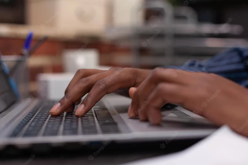 Closeup of african american hands typing business data on portable computer keyboard in startup brick wall office. focus on startup employee using laptop for professional work or composing email. Free Photo