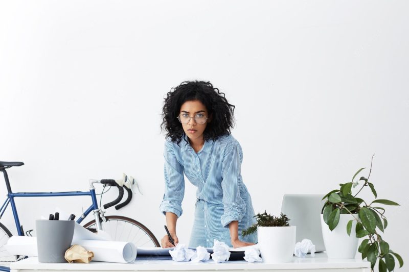 Concentrated African woman writing something on papers, standing in front of table Free Photo