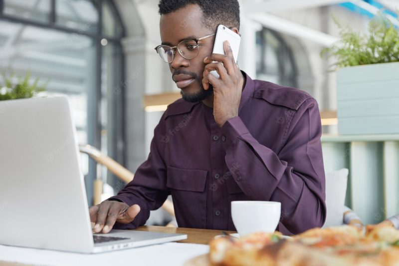 Concentrated dark skinned man in formal wear looks confidently into laptop computer, has serious expression Free Photo