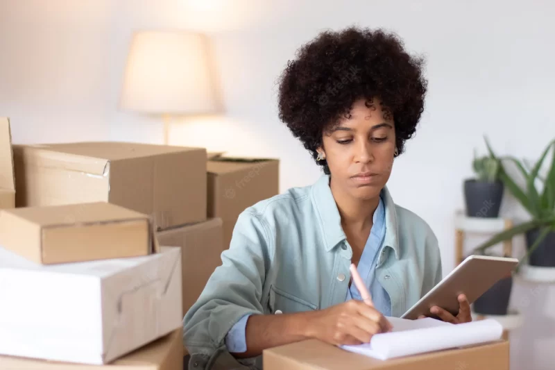 Concentrated woman making notes about package. serious young logistics clerk using digital tablet while working at warehouse. storeroom concept Free Photo