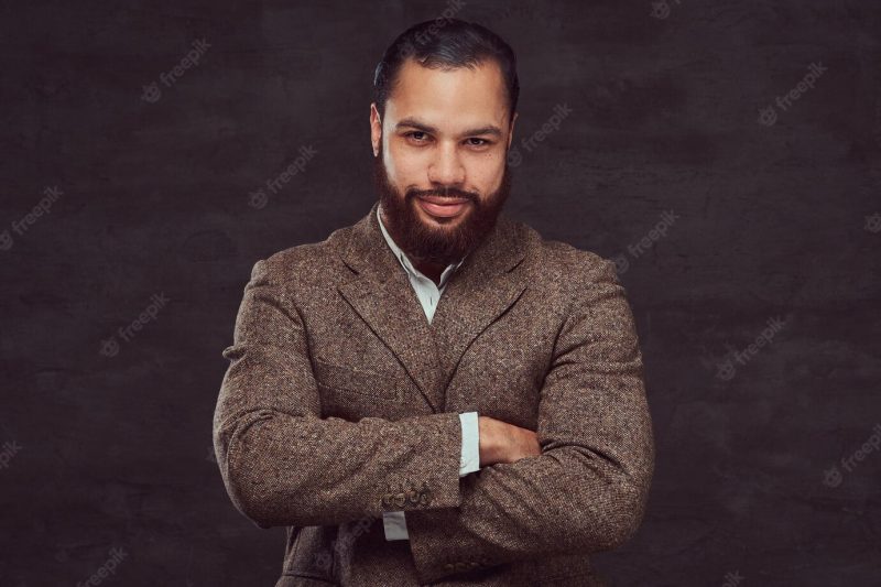 Confident african-american businessman in a brown classic jacket with crossing arms. isolated on a dark background. Free Photo