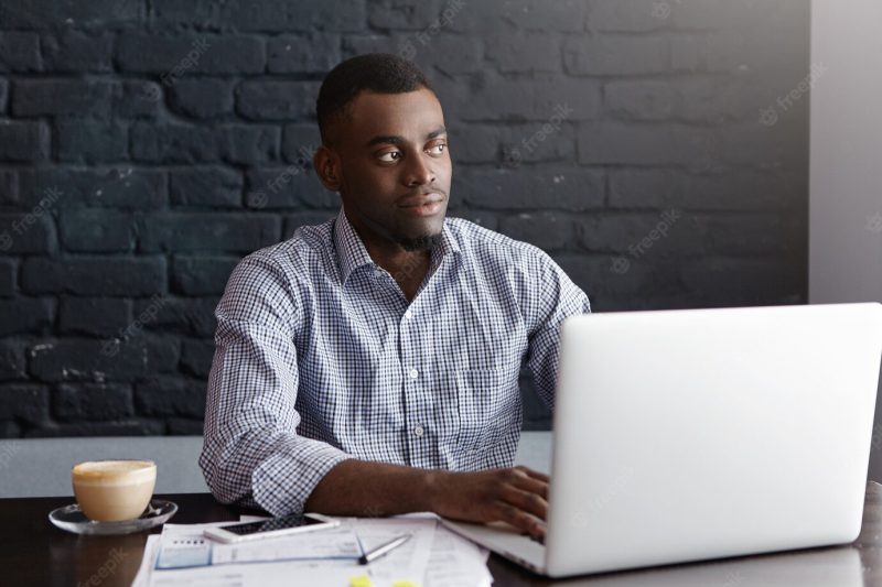 Confident young African entrepreneur sitting in front of open laptop Free Photo