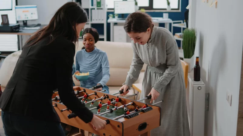 Corporate workmates using foosball table to play soccer game, playing after work at office. colleagues drinking bottles of beer and alcohol while enjoying activity to have fun Free Photo