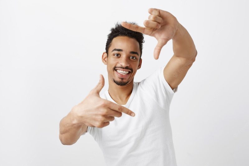 Creative handsome African American man looking through hand frames and smiling, picturing moment Free Photo